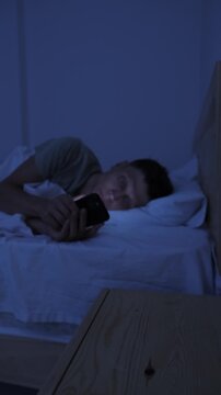 Man compulsively scrolling smartphone in bed at night, struggling with digital addiction, doomscrolling and inability to stop screen time, vertical