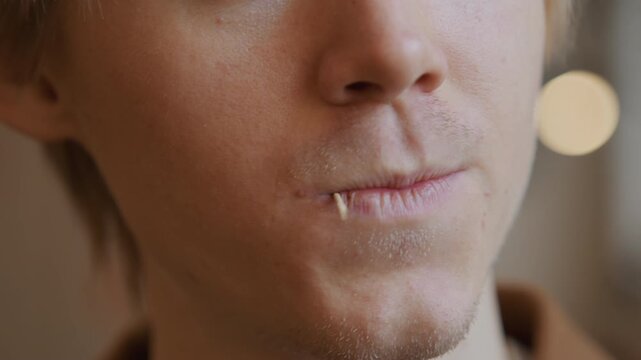 Close up of young man using dental floss to clean teeth with steady hand and visible texture detail. Dental care activity shown in soft indoor lighting focusing on mouth area