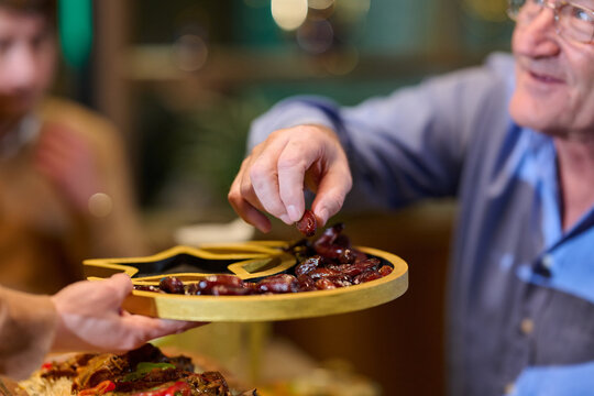 Elder Man Sharing Dates From Decorative Platter At Family Gathering Celebration