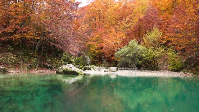 Oko Skakavice, the Blue Eye of Montenegro surrounded by colorful foliage in red, yellow and orange in autumn