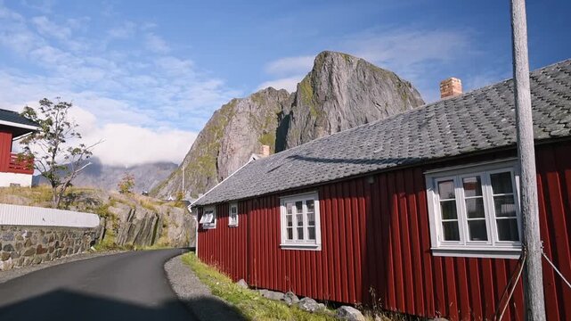 Red timber cabin beside a village lane below a granite dome, Hamnoy, Lofoten, Norway