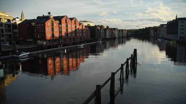 Red timber wharf houses reflected in the calm Nidelva, Trondheim, Trondelag, Norway