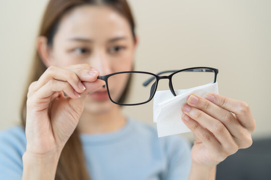 Close-up person cleaning eyeglasses with microfiber fabric.
