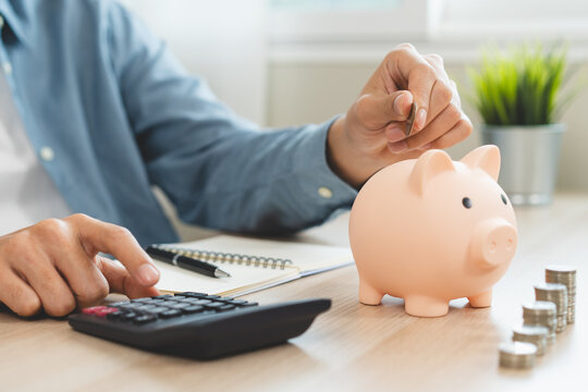 Young woman saving money monthly expenses putting coin in to piggy bank on the table.