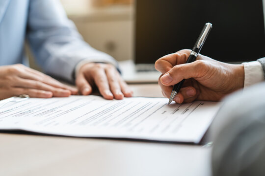Extreme close up of businessman signing official document with black pen.