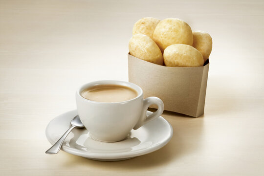 X&iacute;cara de caf&eacute; com leite e por&ccedil;&atilde;o de p&atilde;o de queijo - Cup of coffee with milk and a portion of Brazilian cheese bread on a wooden table