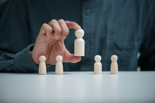 Business professional selects a wooden figure from a group, symbolizing hiring, recruitment, candidate selection, talent assessment, workforce planning and human resources decisions.