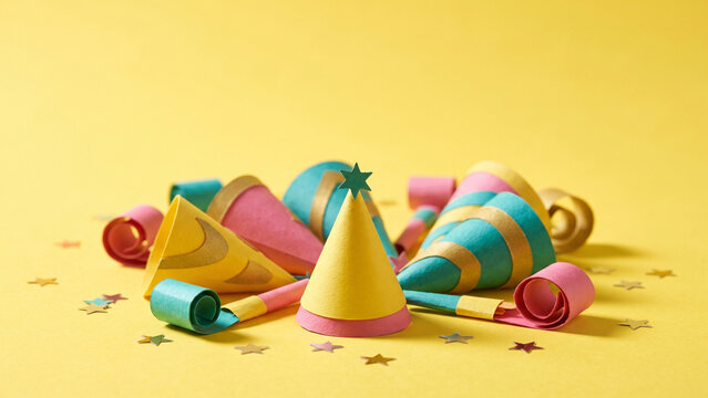 Festive new year celebration with colorful party hats, blowers, and stars on a yellow background.