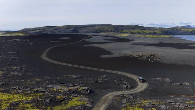 Aerial view of a 4x4 vehicle driving on a winding dirt road through the volcanic black lava fields of Laki with patches of green moss in Skaftarhreppur, Iceland.