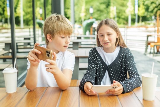 Children Playing Video Games Together on Smartphones at Outdoor Cafe