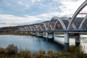 Impressive concrete railway arch bridge crosses water near Jezioro Mucharskie, surrounded by forested Beskid hills in autumn. Repeating arches and vertical hangers create a strong transportation, engi © Volha