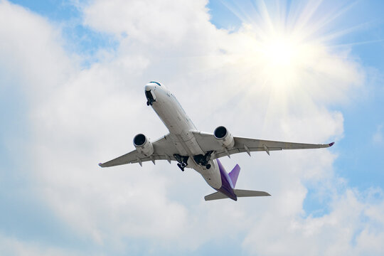 Modern jet airplane soaring high into the atmosphere with landing gear retracting against a backdrop of soft white clouds on a sunny day