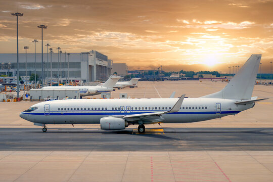 Commercial airliner moving across the tarmac at a busy airport under a clear blue sky while ground crews prepare for daily departure operations
