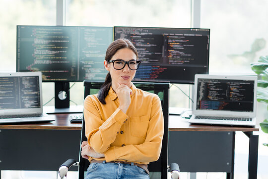 Female software developer in office thinking at her desk with multiple monitors showing code, confident programmer working on coding and web development projects