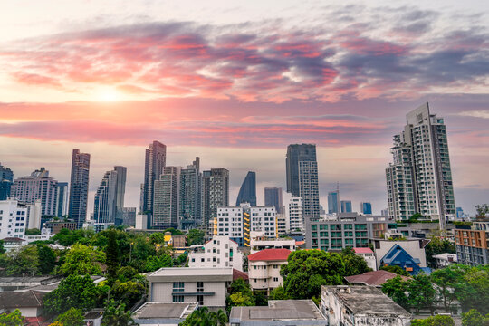 Vibrant sunset clouds drift over the high buildings and residential areas in the busy city center of Bangkok during the late evening golden hour