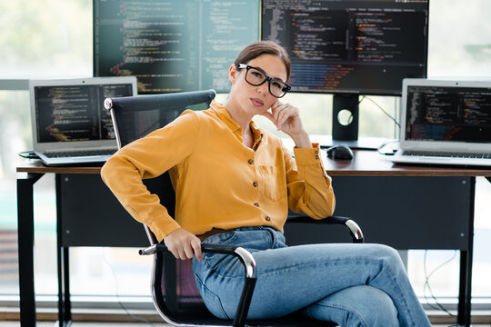 Female programmer working remotely at a modern desk with multiple monitors coding software and analyzing data in a bright office workspace