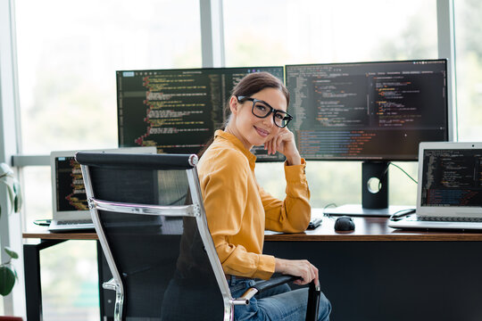 Female software developer smiling at desk with multiple monitors showing code in a bright modern office workspace
