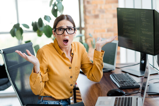 Frustrated woman programmer at office desk reacting in shock to coding error on laptop and monitor while working from home in a modern workspace