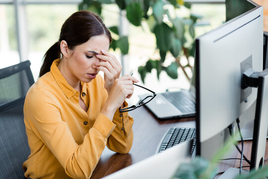 Stressed businesswoman rubbing her eyes at a computer desk during a long workday in a modern office