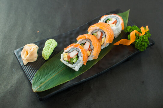 Delicious salmon sushi rolls served with wasabi and ginger on a black plate

