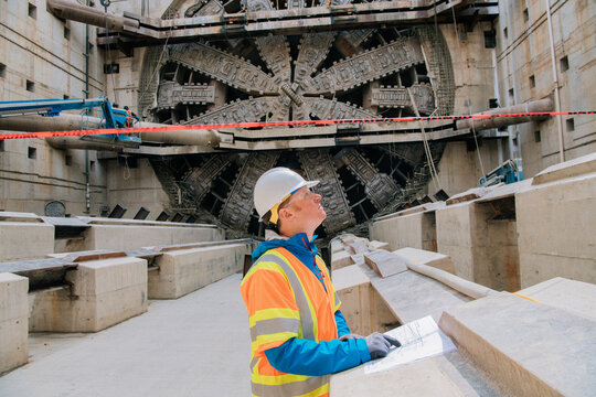 A construction white worker inspects blueprints by a tunnel boring