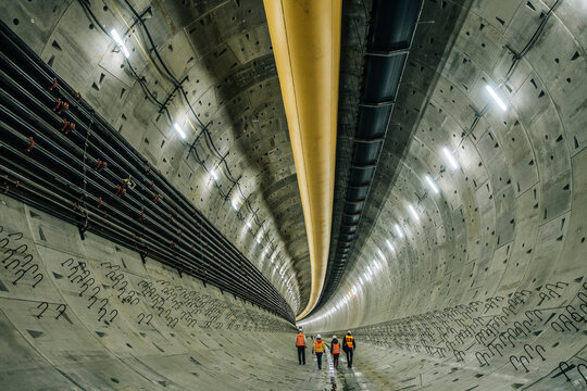 Four workers inspect a large concrete tunnel under construction