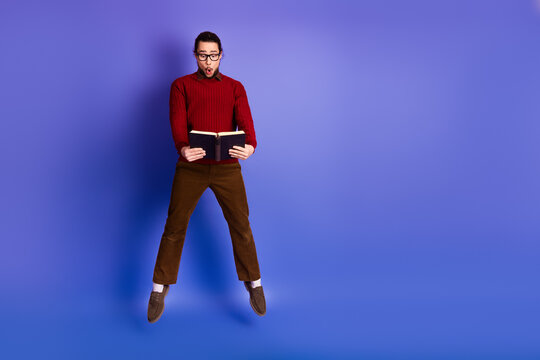 Young handsome man wearing glasses reads a book mid air against violet background in casual study style
