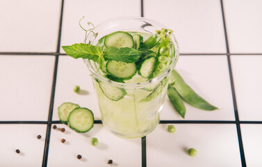A refreshing cucumber peas mint drink in a glass with ice, surrounded by fresh herbs on a rustic...