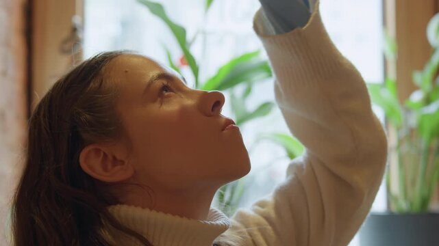 Close up of young woman with long brown hair wearing white turtleneck sweater. Woman raises her right arm and places red ball on top of her head tilting back to look at it. background