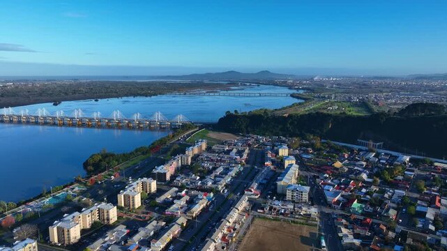 Aerial view of the city of Concepcion, featuring the Bio Bio River and the Juan Pablo II Bridge with urban residential areas and clear blue sky in Concepcion, Bio Bio, Chile.
