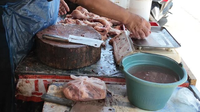 A close-up view highlighting the sharp cleaver slicing through fresh meat on a worn wooden block, complete with a scale and wash basin ready on the side.