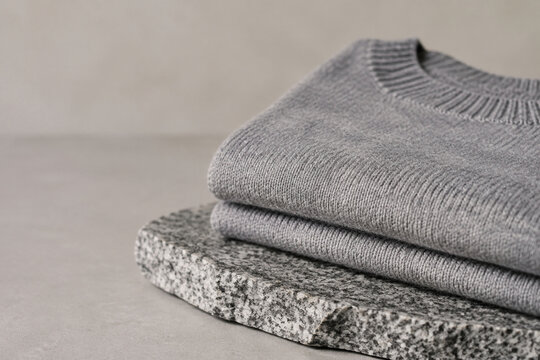 Folded grey sweater on stone slab, cozy knitwear and natural texture concept