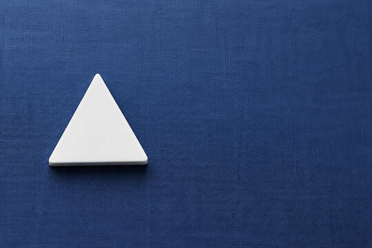 Single white equilateral triangle object on deep blue linen, calm still life for editorial concept
