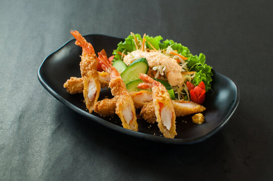 Crispy deep fried breaded ebi fry shrimp served with fresh salad on a black plate
