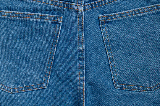 Blue jeans pocket detail shows orange stitching, denim weave, and curved seam in close-up. Cotton textile texture suits apparel marketing, fashion education, product catalogs, and design.