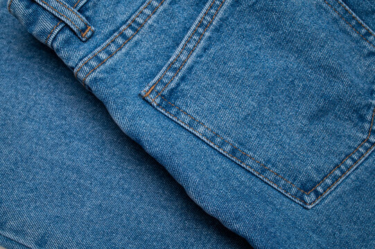 Blue jeans pocket detail shows orange stitching, denim weave, and curved seam in close-up. Cotton textile texture suits apparel marketing, fashion education, product catalogs, and design.