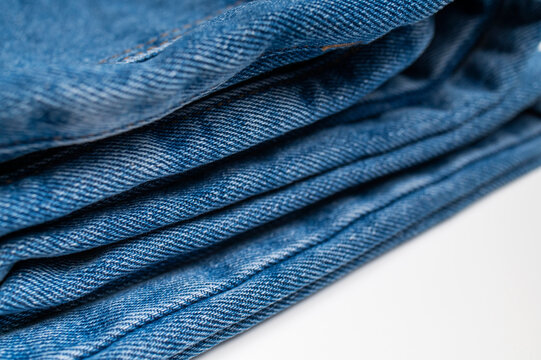 Stacked denim cloth reveals layered blue folds, fine twill weave, and tactile cotton surface. Textile material supports apparel development, craft instruction, retail graphics, and visual branding.