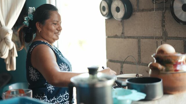 Happy latin woman preparing food with pots in a rustic kitchen while smiling and talking with her family
