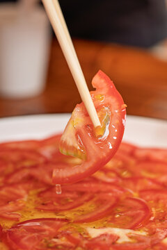 Close up of wooden chopsticks picking fresh tomato slice for Chinese home cooked dish