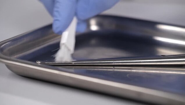Medical professional cleaning surgical forceps in stainless steel tray