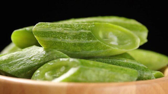 Sliced cooked snake gourd in a wooden bowl slowly rotating on a black background.