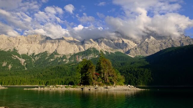 Cinematic video shot of the Zugspitze mountains and a small forest island on the Eibsee lake in the Bavarian Alps, Germany at sunset.