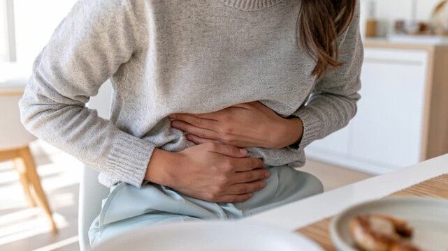 Young Woman Sitting at Dining Table Experiencing Stomach Ache and Abdominal Discomfort After Eating