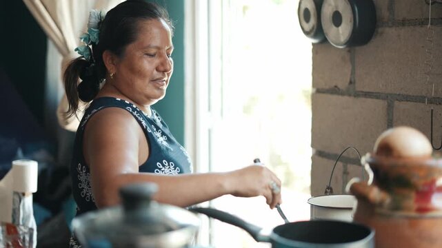 Happy mature latin woman cooking with a pan on the stove in a rustic kitchen at home