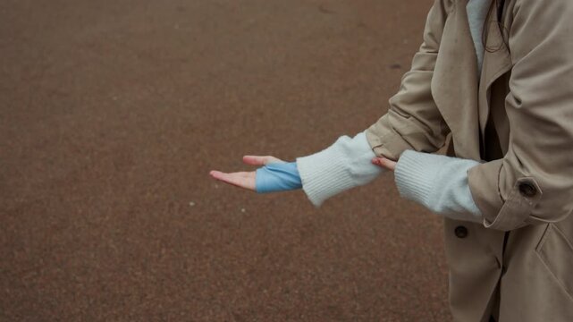 Close up of young woman adjusting her white knit sweater sleeves over blue arm warmers while wearing beige coat focusing on hand movements and clothing details. scene is set outdoors