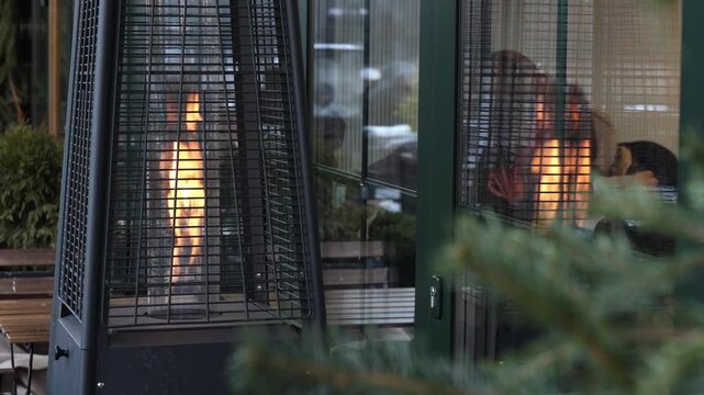 Close-up of outdoor gas heater with burning flame on cafe terrace in evening