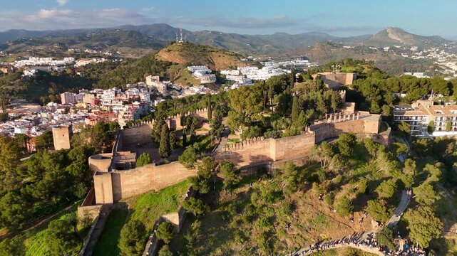 Aerial panorama aerial view of Gibralfaro Castle historic fortress in Malaga, Spain, showing defensive wall, outer fortress wall, and pine covered hill. Orbit parallax shot