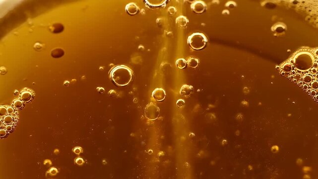 Close-up macro photography of golden amber liquid bubbles rising in a glass drink with sparkling carbonation texture and warm light reflections