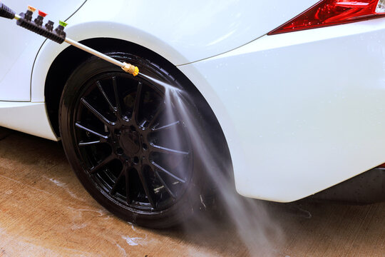 Water sprays from pressure washer cleaning black wheel of white car at car wash