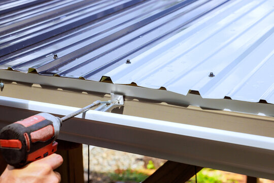 Worker attaches metal gutter to roof using power drill